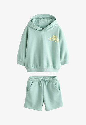 Hellgrüner Hoodie mit dem gelben Schriftzug "BIG SMILES", ausgestattet mit einer Kapuze mit Kordelzug und elastischen, gerippten Bündchen. Kombiniert mit passenden Shorts.