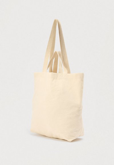 Μπέζ πάνινη τσάντα ώμου με δύο επίπεδες λαβές, ορθογώνιο σχήμα και ομοιόμορφη υφή. Χωρίς εμφανή λογότυπα ή σχέδια. Ενισχυμένες ραφές στις λαβές.
