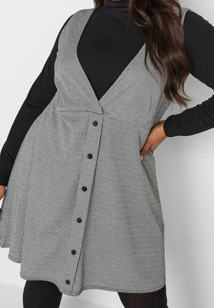 Czarna i biała sukienka w kratkę z dekoltem w kształcie litery V, bez rękawów, z zapięciem na guziki. Stylizowana na czarnym golfie, z rozkloszowanym dołem.