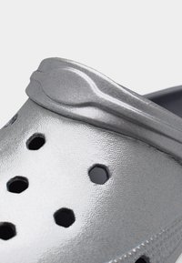 Κοντινό πλάνο ασημί παπουτσιού κλογκ χωρίς κορδόνια με οπές αερισμού και υφασμένο λουράκι στο μπροστινό μέρος.