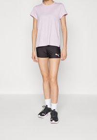Světle růžové tričko s krátkým rukávem spárované s černými sportovními šortkami. Černé a růžové sportovní boty, bílé kotníkové ponožky. Jednoduchý design, funkční střih.