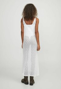 Vestido largo de encaje blanco con un corsé ajustado y una falda larga y suelta. Presenta un patrón geométrico y tirantes finos.