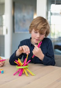 Bastoncini di plastica colorati in rosa, giallo e verde sono impilati in un ordinato disordine, mentre un bambino interagisce con i pezzi.