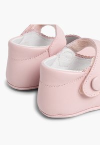 Zapatitos de bebé de cuero rosa con un diseño redondeado, cuentan con una correa de velcro para el cierre y un interior suave y acolchado. Textura lisa en toda la superficie.