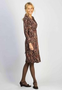 Mekko on burguuninvärinen ja beige paisley-kuvio, pitkät hihat, kapeampi vyötärö ja se ulottuu polven alapuolelle. Ruskeat matalat korkokengät.