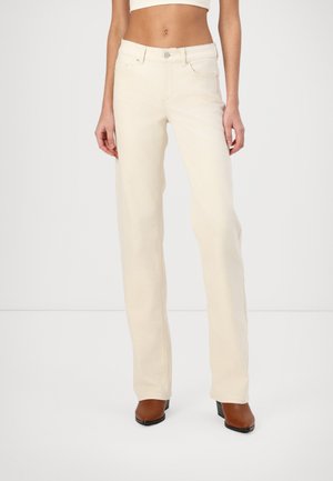 Helle beige Straight-Leg-Jeans mit fünf Taschen, Knopfverschluss und dezenten Nähdetails. Kombiniert mit braunen High-Heels-Stiefeln.