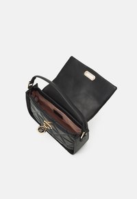 Schwarz gesteppte Handtasche mit goldenen Beschlägen, strukturierter Form und einer strukturierten Lederaußenseite. Offener Klappeneingang, der ein braunes Innenfutter zeigt.