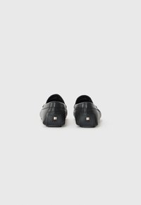Cărăbușe negre din piele, slip-on, cu un finisaj texturat, având un accent logo pătrat pe toc și un design cu vârf rotunjit.