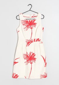 Vit klänning med röda blommönster, ärmlös design, figursydd midja och utsvängd kjol. Hänger från en svart metalhängare.