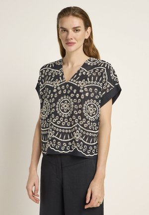 Navy blouse with V-neck and short sleeves, featuring intricate white floral embroidery and scalloped hem detail. Soft, lightweight fabric.