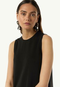 Czarna bezrękawnik o gładkiej fakturze, okrągłym dekolcie i luźnym kroju. Wyraziste, duże srebrne kolczyki. 