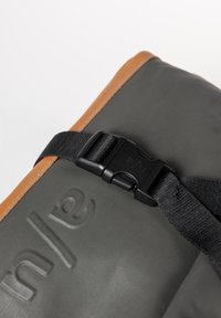 Gray bag with a textured finish, featuring a black plastic buckle and brown leather accents. The brand name is embossed on the surface.