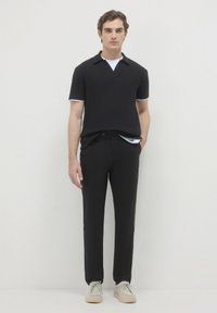 Polo nero con bordi bianchi, abbinato a pantaloni neri. L'outfit presenta una vestibilità slim ed è completato da sneakers grigio chiaro.