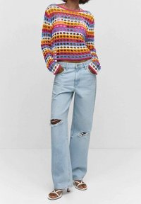 Pull en maille multicolore avec des découpes circulaires, associé à un jean large d écontracté bleu clair délavé avec deux déchirures aux genoux.