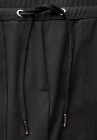 Svarta joggers har en dragsko i midjan med silverfärgade öglor, en slät yta och sidofickor för funktionalitet.