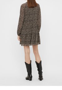 Robe noire à fleurs avec manches longues transparentes, jupe à volants et encolure ronde. Associée à des bottes en cuir noires montantes jusqu'aux genoux.