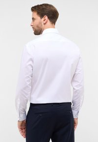 Weißes Langarmhemd mit Kentkragen, glatter Textur, knopfbaren Manschetten und schlichtem Design, kombiniert mit dunkelblauen Hosen.