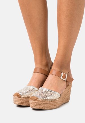 Sandales à plateforme compensée en jute tissé, finition dorée scintillante sur l'avant-pied, et bride de cheville marron ajustable pour un maintien sécurisé.
