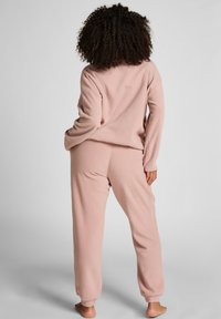 Lichtroze fleece loungewear set met een relaxte pullover en bijpassende joggerbroeken met geribbelde boorden en een zachte textuur.