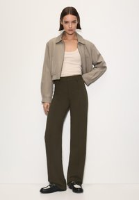 Beskaaret beige bomberjakke båret over en tætsiddende cremefarvet tanktop, parret med høj talje, lige ben i olivengrønne bukser og sorte sko.