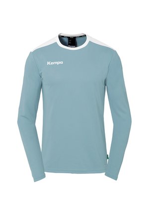 Maglietta sportiva a maniche lunghe di colore azzurro chiaro con dettagli bianchi. Realizzata in tessuto leggero, presenta un colletto arrotondato e il logo "Kempa" in bianco.