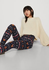Marineblå leggings med vintertema, inkludert snøfnugg, pepperkakemenn og godteristenger. Myk, elastisk stoff med en behagelig passform.