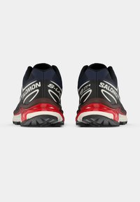 Παπούτσια Salomon S-Lab XT6 σε ναυτικό μπλε, μαύρο και κόκκινο. Διαθέτουν υφασμένη σόλα από καουτσούκ, επένδυση στον περιμετρικό σωλήνα και λογότυπα σε αντιθετικά χρώματα στις πλευρές.