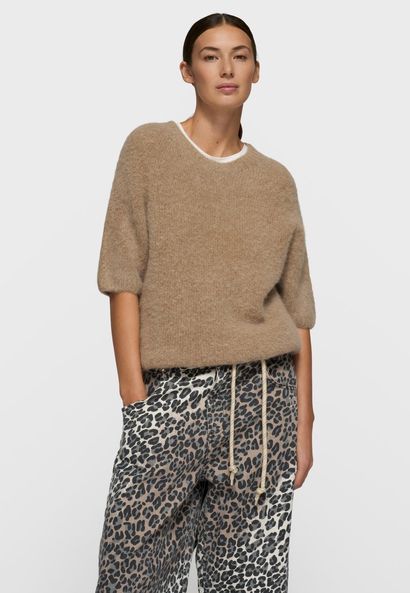 Pull en tricot beige avec manches courtes bouffantes et encolure arrondie, associé à un pantalon ample à imprimé léopard avec taille élastique et cordon de serrage.