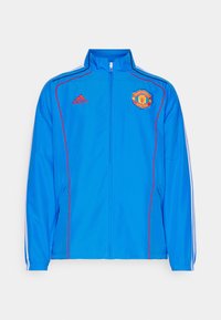 Modra športna jakna z logotipom Manchester United, rdečimi poudarki in belimi črtami na rokavih. Izdelana iz lahkotnega materiala.