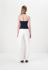 Mornarica halter top s uskim dizajnom, uparen s ležernim, visokim bijelim hlačama. Glatka tekstura i minimalistički stil.