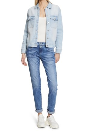 Světle modrá džínová bunda se dvěma náprsními kapsami a stříbrnými knoflíky, v kombinaci se světle modrými džíny a bílými teniskami. Uvolněný střih a ohrnuté rukávy.