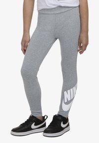 Grå leggings med tettsittende passform, med en stor hvit "NIKE"-logo på nedre venstre ben. Brukes med svarte joggesko.