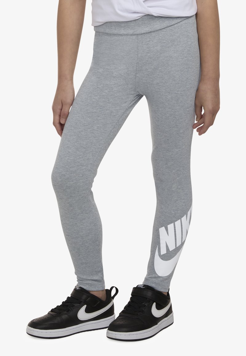 Grå leggings med tettsittende passform, med en stor hvit "NIKE"-logo på nedre venstre ben. Brukes med svarte joggesko.