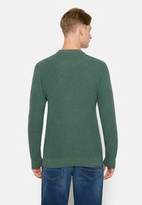 Pulover verde texturat cu mâneci lungi și guler rotund, asociat cu blugi albaștri. Materialul pare tricotat cu benzi ribbate la margini.