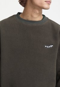 Ciemnozielony polarowy sweatshirt z okrągłym dekoltem, z małym białym logo "VOLCOM" na lewej piersi. Miękka tekstura i luźny krój.