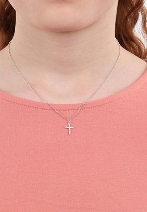 Silberne Kettenhalskette mit einem kleinen, schlichten Kreuzanhänger. Der Anhänger hat eine strukturierte Oberfläche. Er wird über einem hellrosa Oberteil getragen.