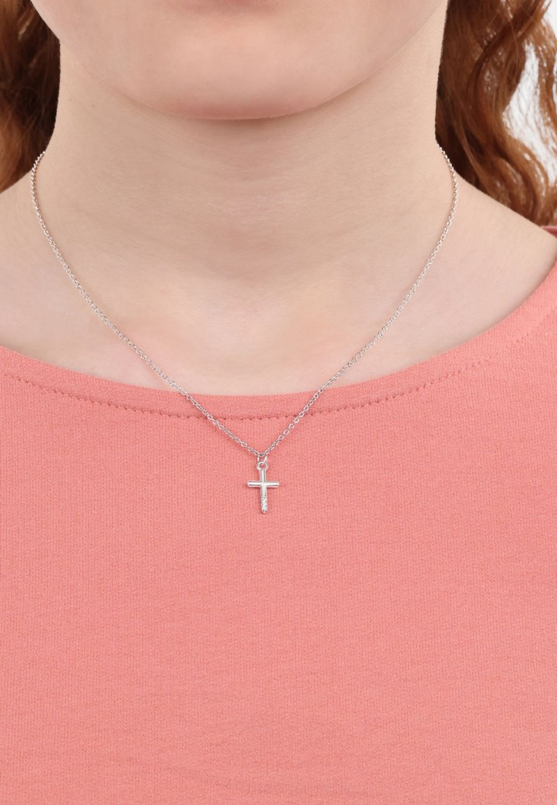 Zilveren ketting met een kleine, eenvoudige kruis hanger. De hanger heeft een gestructureerd oppervlak. Draagt boven een lichtroze top.