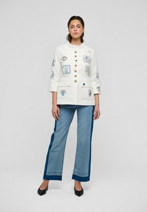 Hvid bomuldsjakke med broderede mærker i blå og pink, guldknapper og to forlommer; kombineret med højtaljede flared jeans.