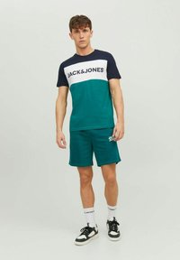 Green and navy JACHS&JONES short-sleeve t-shirt with a white logo, paired with matching green shorts. Black and white sneakers complete the look.
