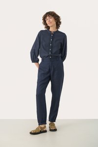 Camicia di lino blu navy con maniche a sbuffo e chiusura a bottoni. Abbinata a pantaloni in lino blu navy e sandali con cinturini di colore verde oliva.