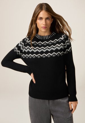Suéter negro de punto con un patrón geométrico gris en los hombros y un cuello redondo adornado con tachuelas plateadas. Mangas largas y puños acanalados.