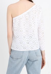Hvid off-the-shoulder top med broderet hulmønster, langærmet på den ene side, elastisk halsudskæring og afslappet pasform.