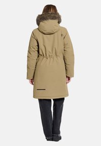 Langer beiger Parka mit einem mit Fell gefütterten Kapuzen, Kordelzug an der Taille und schwarzen Akzentdetails am Saum. Glatte Textur und knielanges Design.