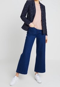 Námořnický blejzr s malými bílými vzory, světle růžový svetr, široké tmavé džíny a bílé tenisky. Ležérní a moderní outfit.