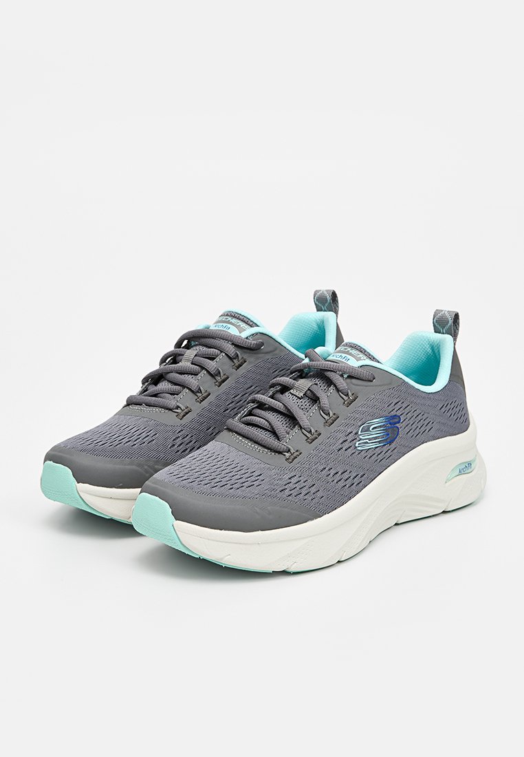 Zapatillas deportivas grises con una parte superior de malla texturada, acentos en azul claro y una suela blanca acolchada. Presenta cordones y una marca en el lateral.