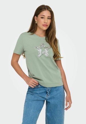 Lys grøn kortærmet T-shirt med et sølvfarvet pailletstjernedesign på forsiden, parret med højtaljede blå denim jeans.