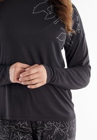 Person wearing a black long-sleeve top with white floral line designs and matching black pants with white floral patterns.