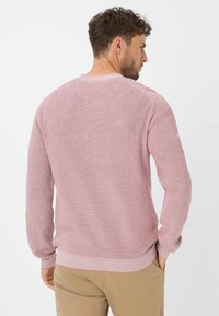 Gestructureerde, lichtroze trui met ribbelbreisel en ronde hals. Heeft lange mouwen en een aansluitende onderkant, weergegeven vanuit de achterkant.