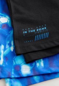 Tissu noir avec texte bleu indiquant "GAME OVER IN THE ZONE LEVEL" superposé sur un tissu à motif balle de football bleu et blanc.