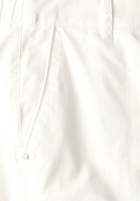 Valkoinen puuvillakangas, jossa on sileä pinta, ommellut saumat ja sivutasku, jossa on pieni metallinappikoristus.